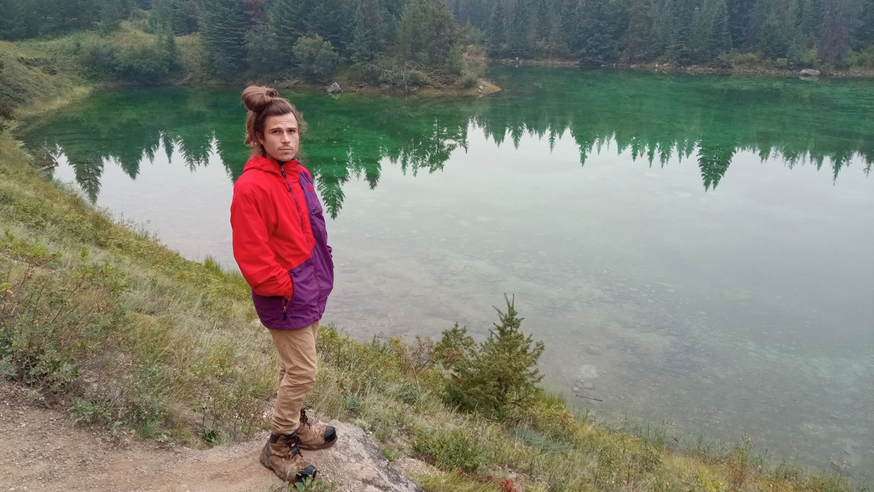 Layf standing beside a green mountain lake surrounded by pine trees